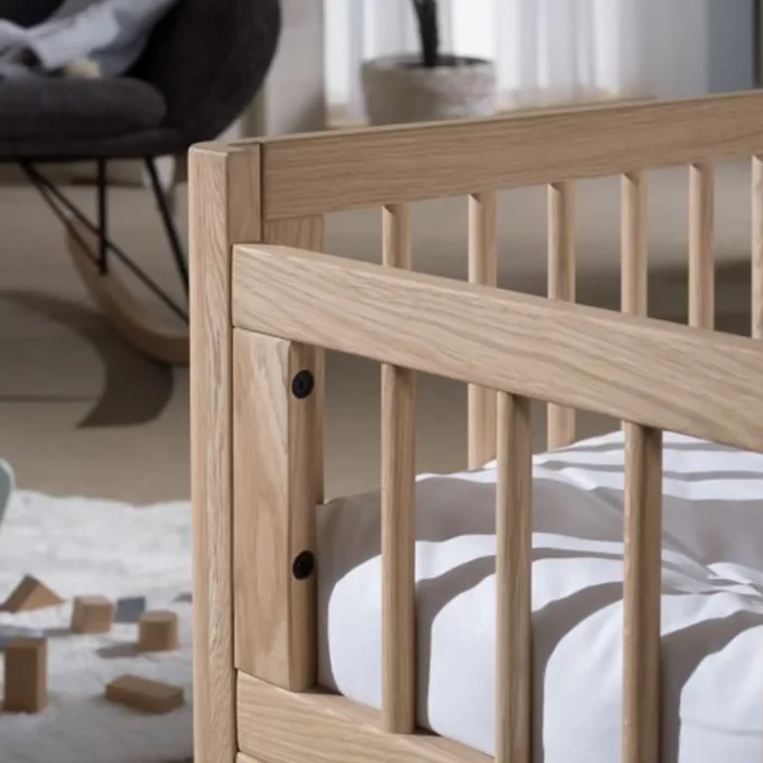 Ein Vipack Junior Holz-Kinderbett Forrest Eiche mit weißer Matratze steht in einem Raum mit einem Stuhl und verstreuten Holzklötzen auf dem Boden.