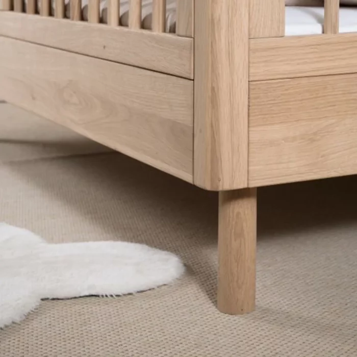 Nahaufnahme des Vipack Junior Holz-Kinderbetts Forrest Eiche Ecke mit zylindrischen Beinen auf einem beigen Teppich neben einem weißen, wolkenförmigen Teppich.